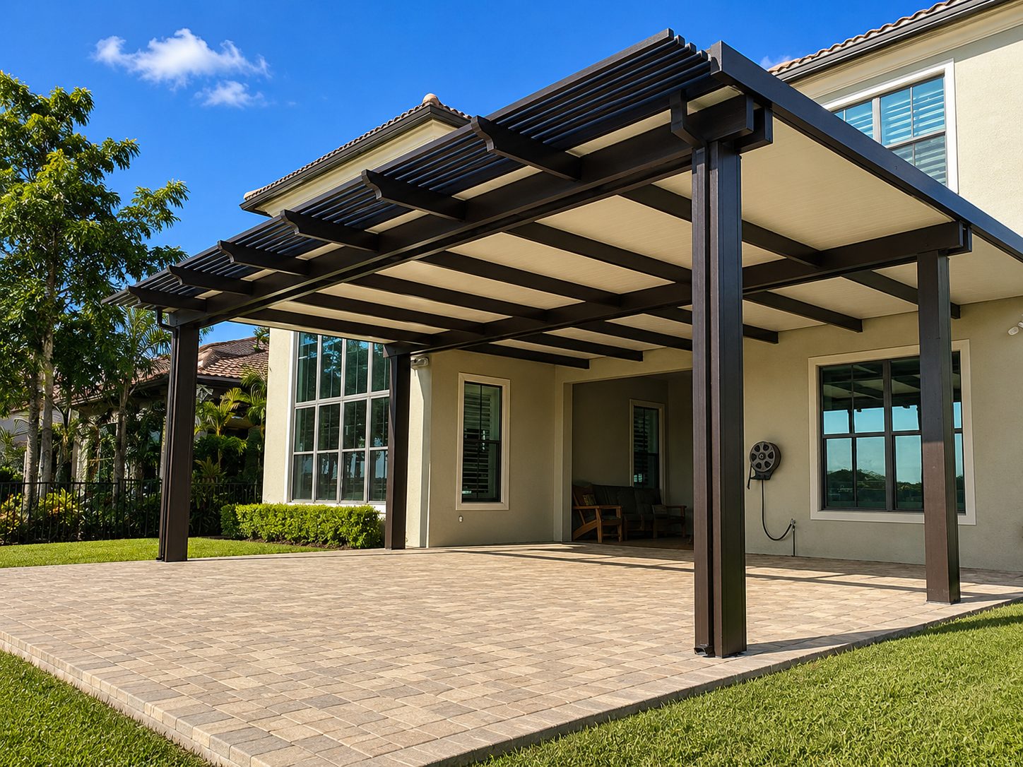 Wide bronze aluminum patio cover with open rafter ends over a paver patio at the back of a home